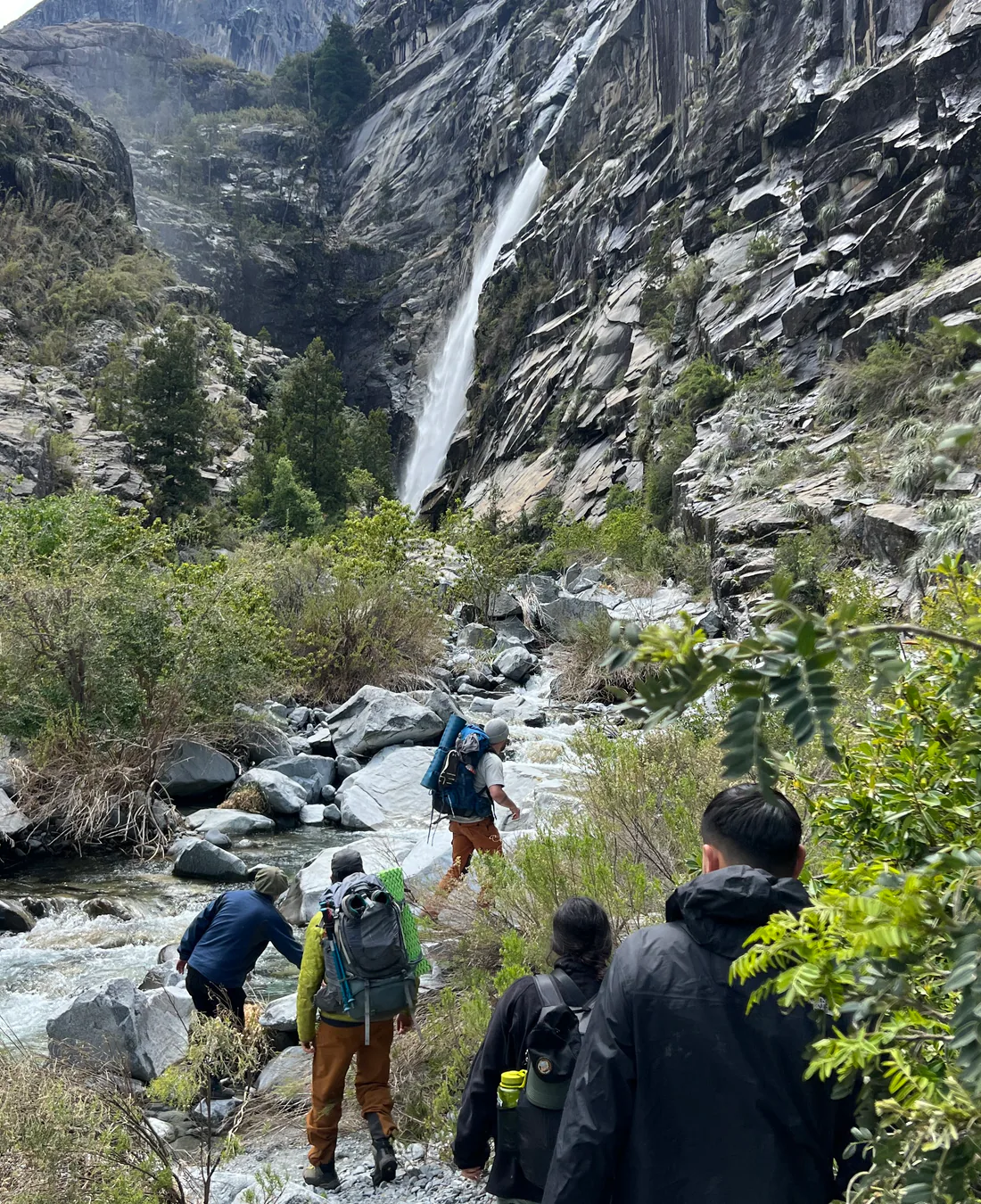 Grupo de caminantes avanzando junto a un curso de agua de montaña